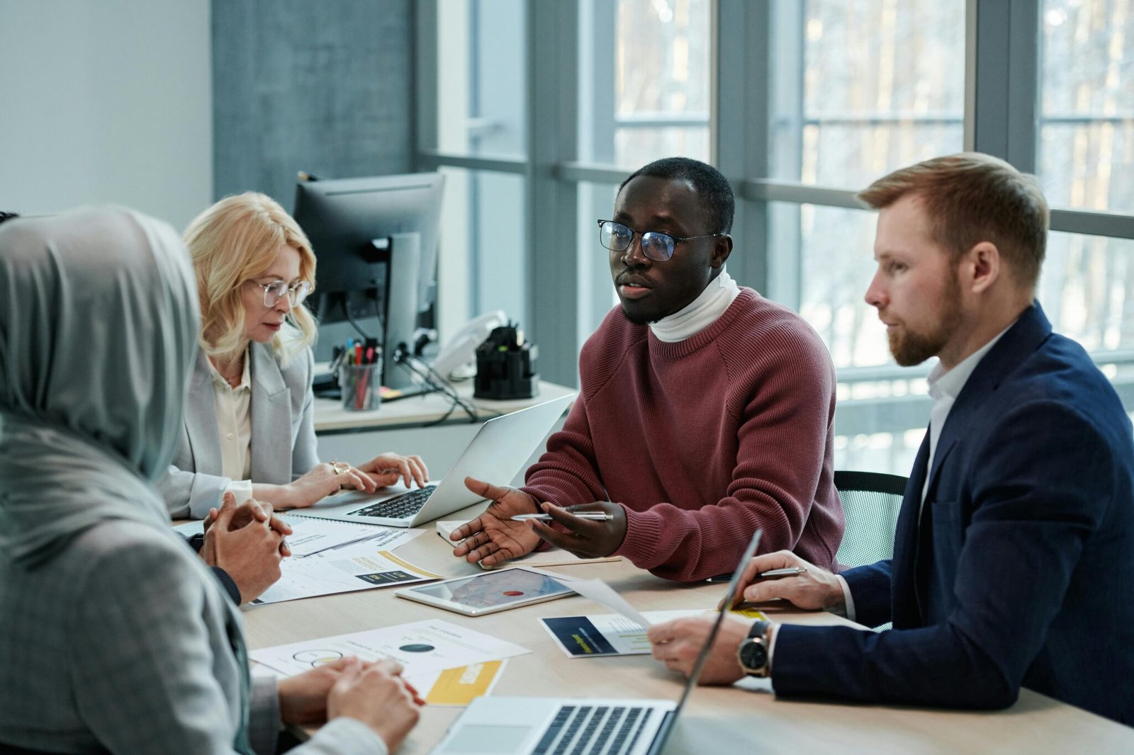 A diverse group of professionals having a meeting in a modern office setting with laptops and papers.